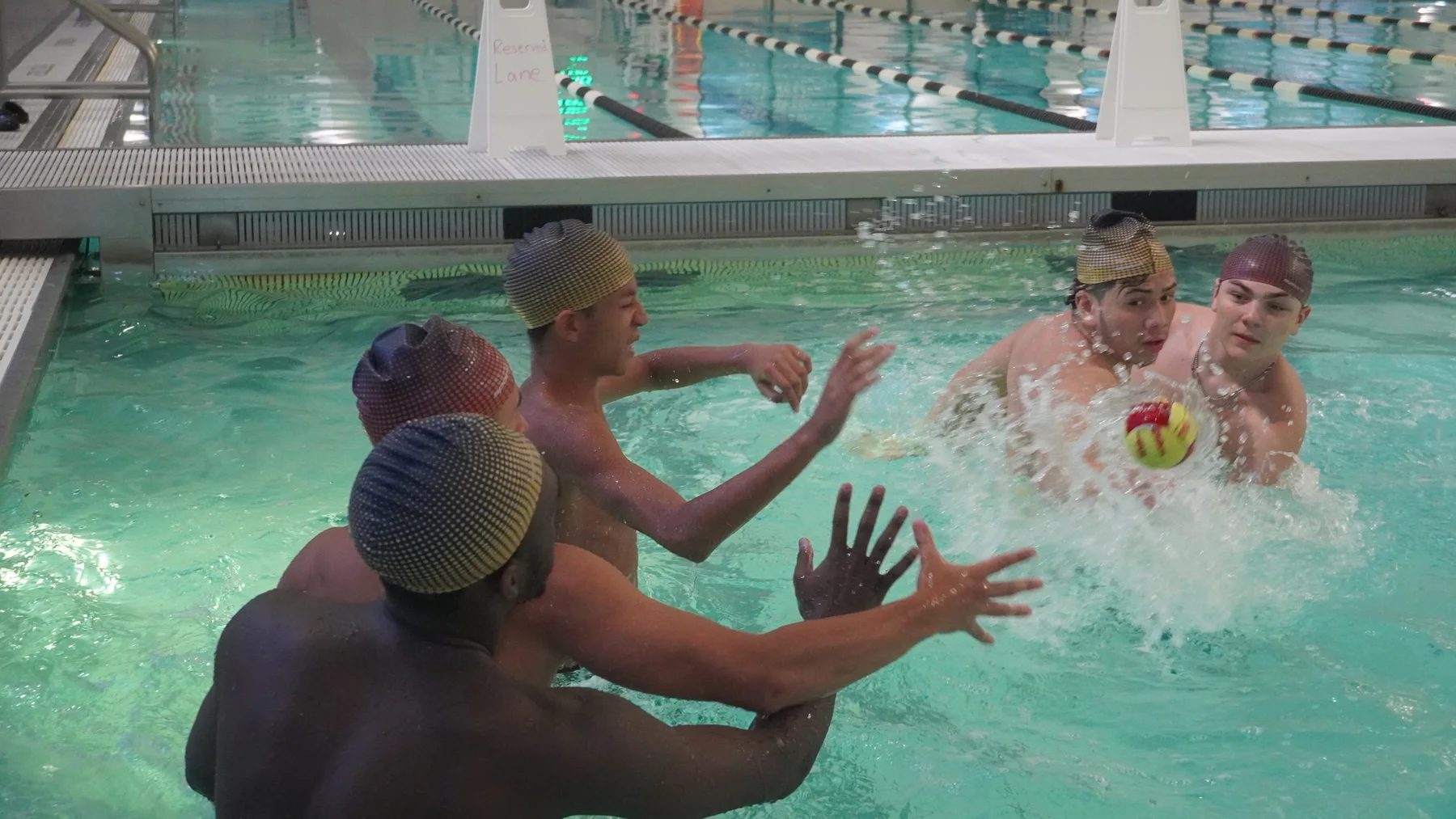 Players reach toward a ball amid splashing water.