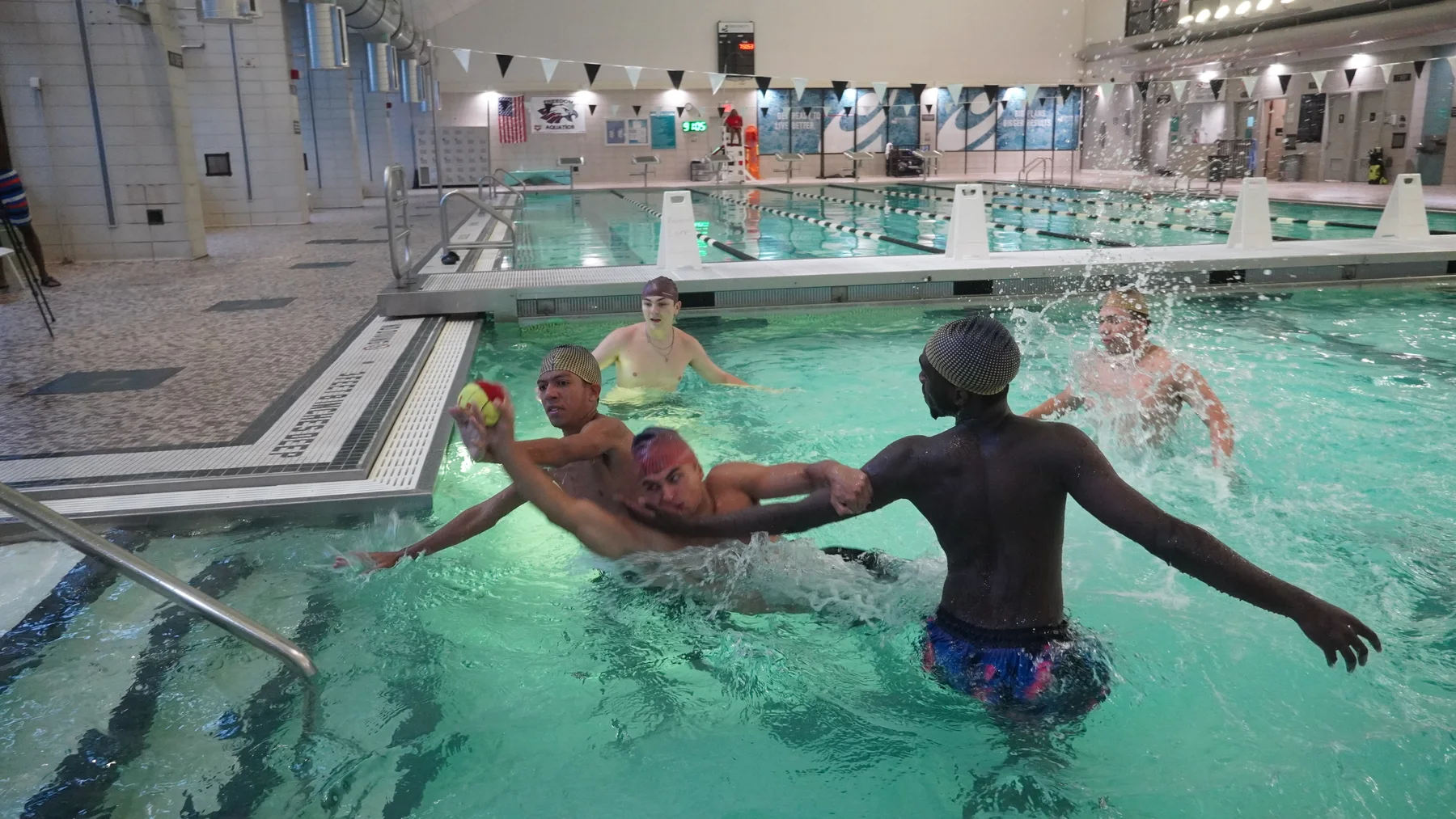 Players reach and move around one another as a player holds the ball in the pool.
