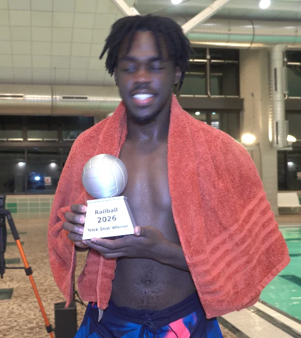 A participant wrapped in an orange towel holds a Railball trophy.